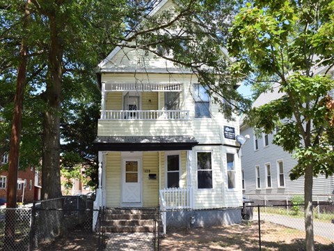 A white two-story house with a porch and a tree in front.