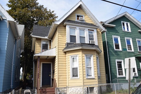 A yellow house with a black door and a window is in front of a green house.