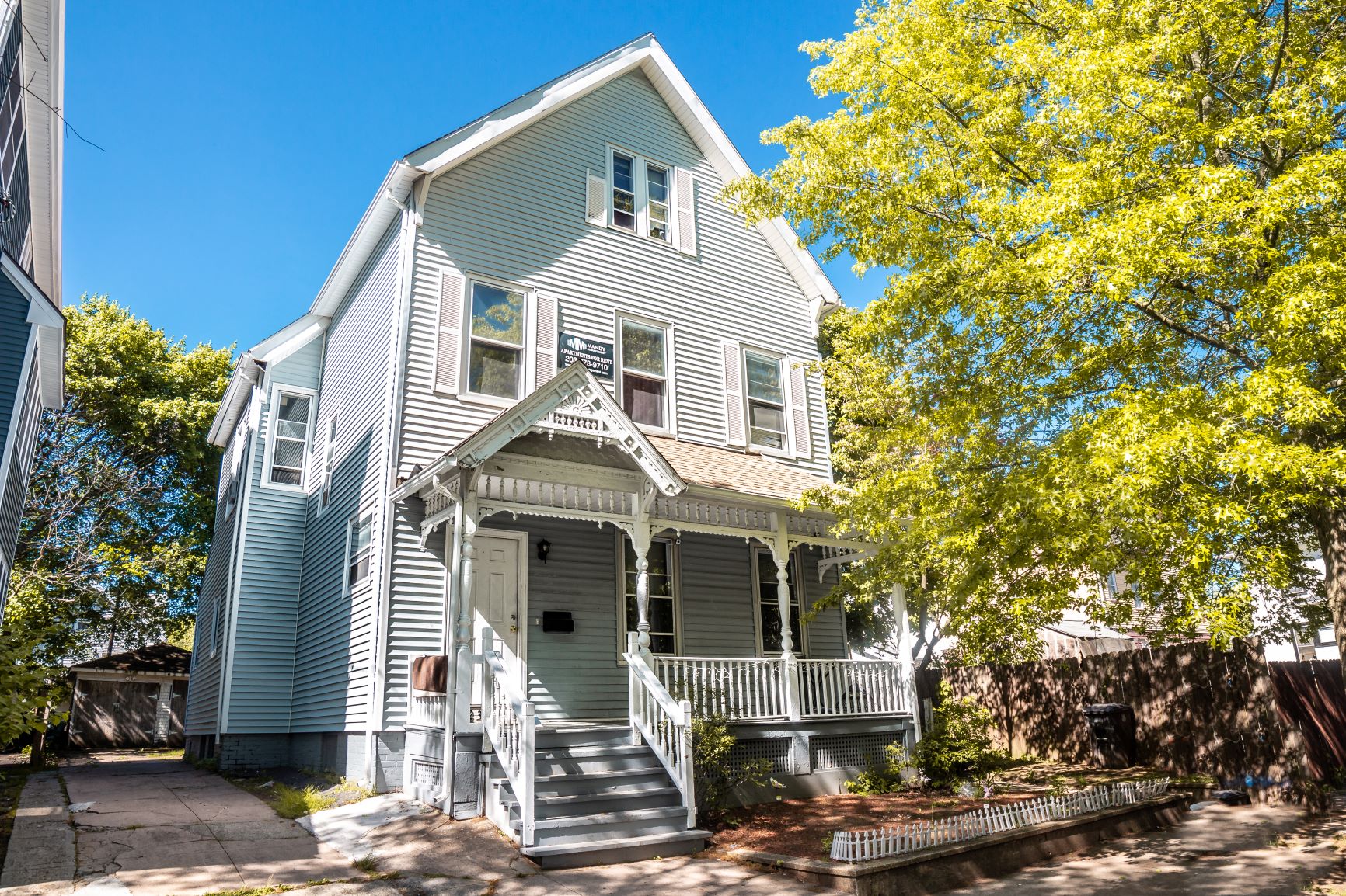 A two-story house with a front porch and a tree in front.