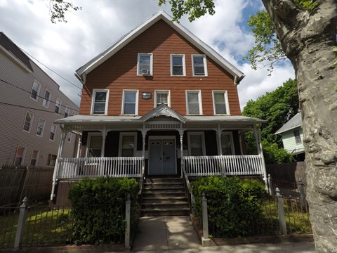 A brown house with a white fence and a green bush in front.