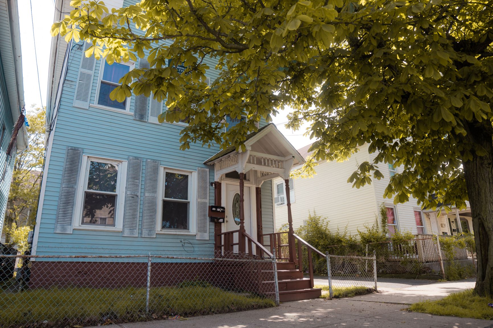 A blue house with a white porch and a tree in front.