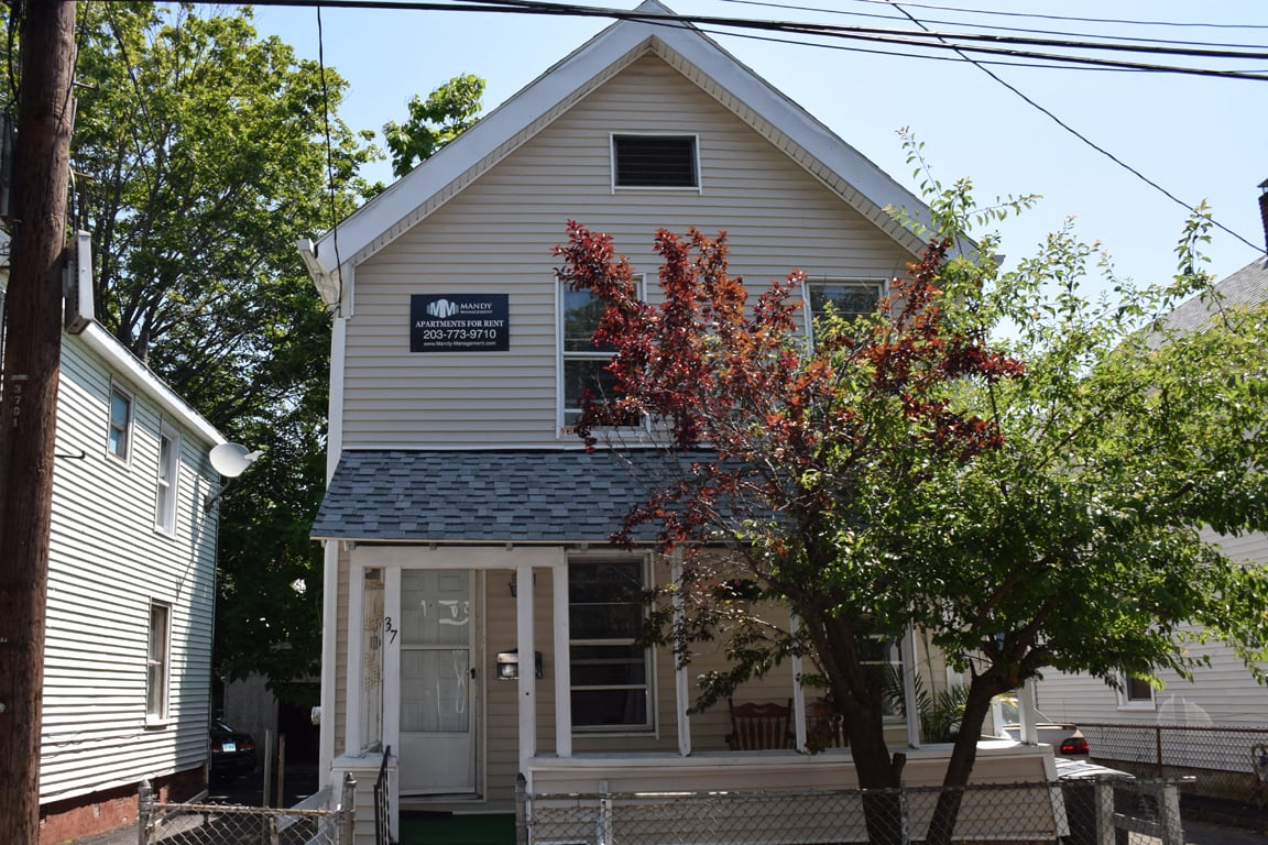 A small house with a porch and a tree in front.