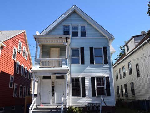 A white house with a balcony sits between a red house and a beige house.