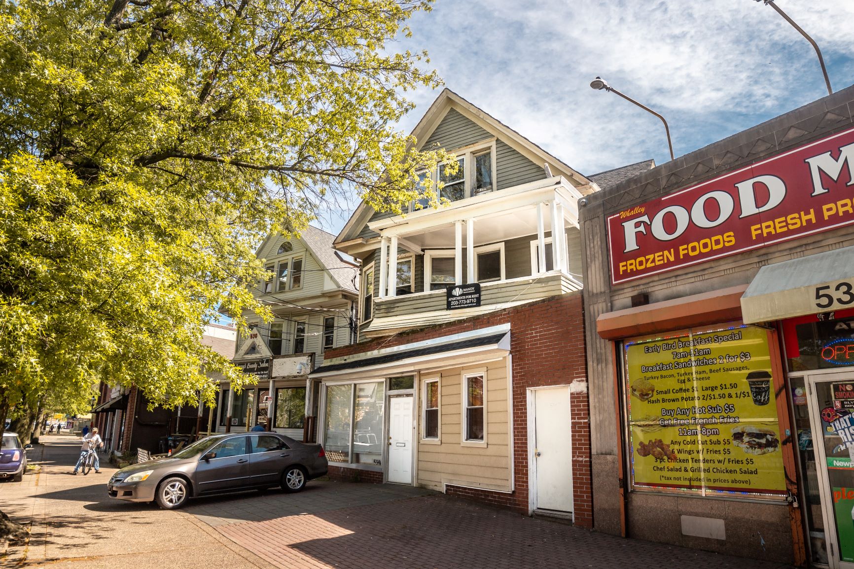 A street view with a car parked in front of a building with a sign that says "Food M".