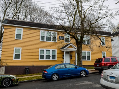 A blue car is parked in front of a yellow house.