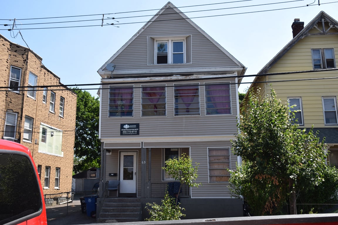 A grey house with a red car parked in front.