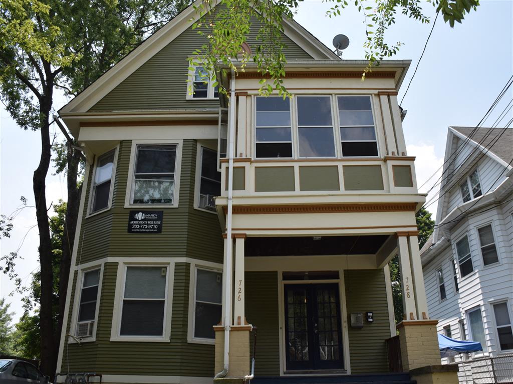 A green two-story house with a balcony on the second floor.