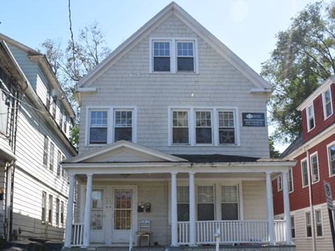 A white house with a porch and a sign on the front.