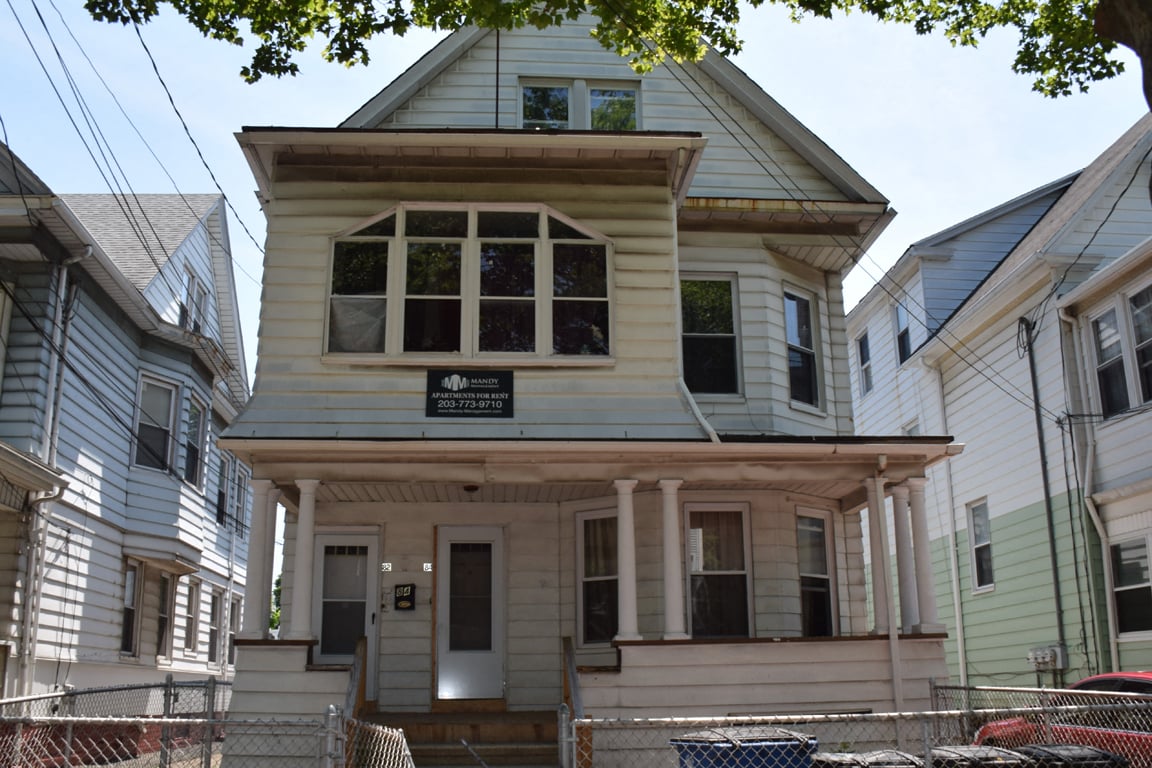 A house with a sign that says "For Sale" is in front of other houses.