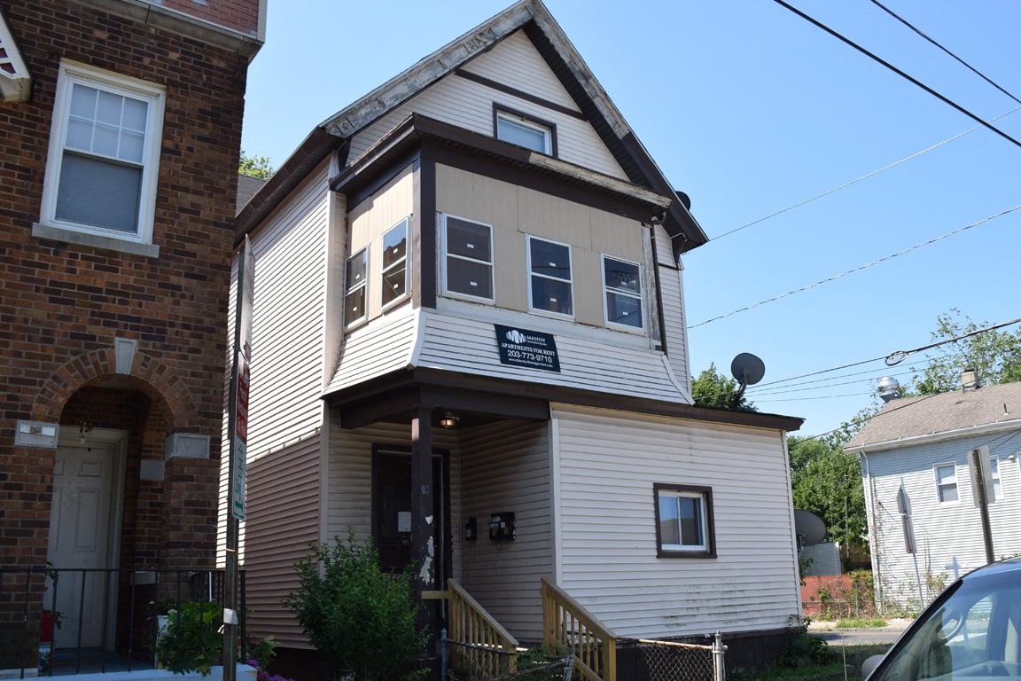 A house with a brown and white exterior and a black sign on the front.