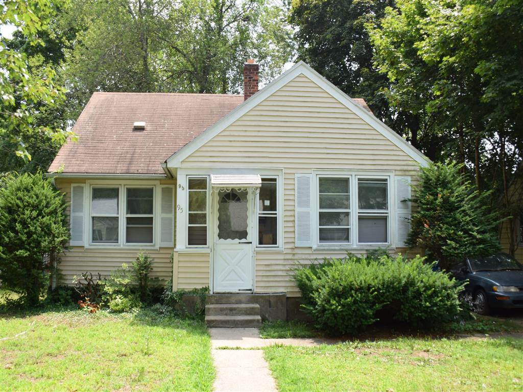 A small house with a white door and windows surrounded by greenery.