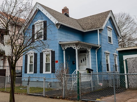 A blue house with a white door and a fence in front.