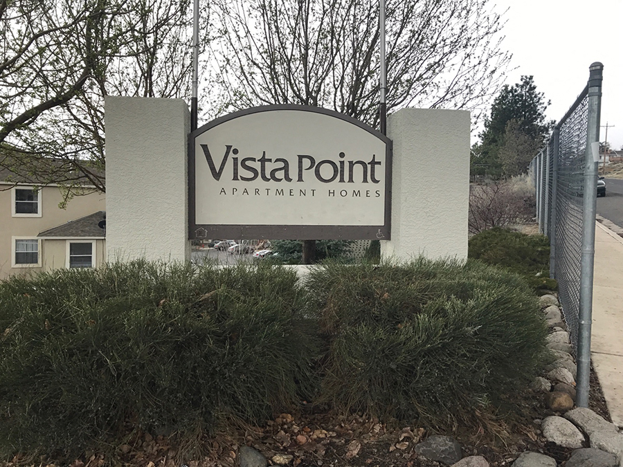 A sign for Vista Point Apartment Homes is displayed in front of a fence and some bushes.