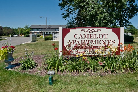 a sign for camlot apartments in front of a yard with flowers