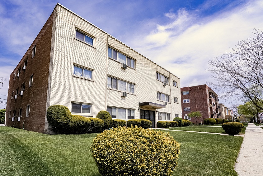 a brick apartment building with green grass and bushes