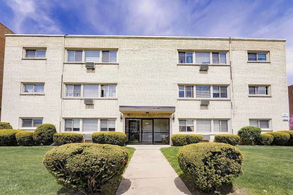 a white brick apartment building with a sidewalk and bushes in front of it