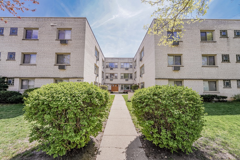 a walkway between two apartment buildings with green bushes