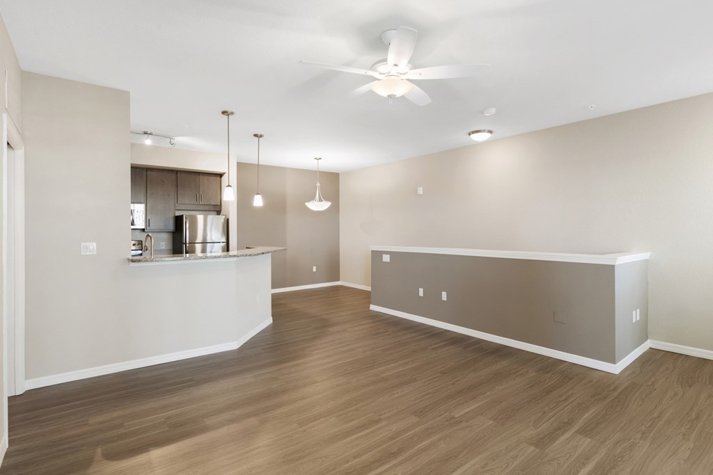 an empty living room with a kitchen and a ceiling fan