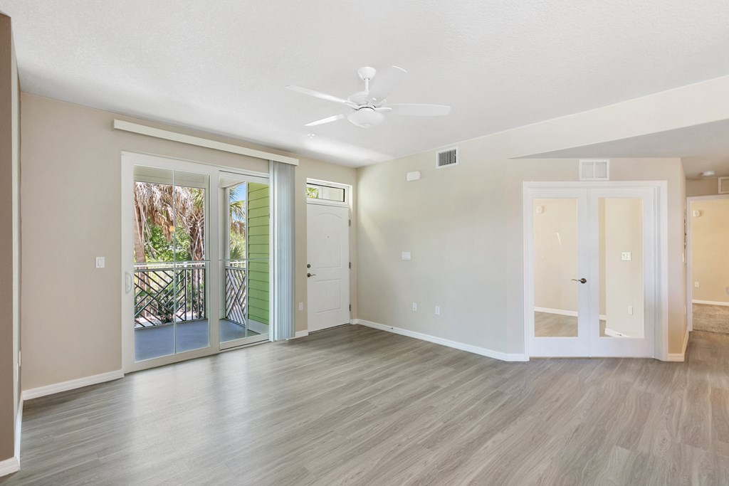 an empty living room with a ceiling fan and doors to a balcony