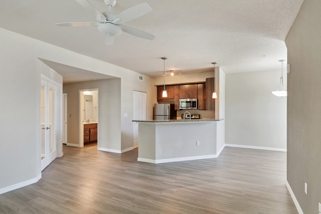 an empty living room with a kitchen and a ceiling fan