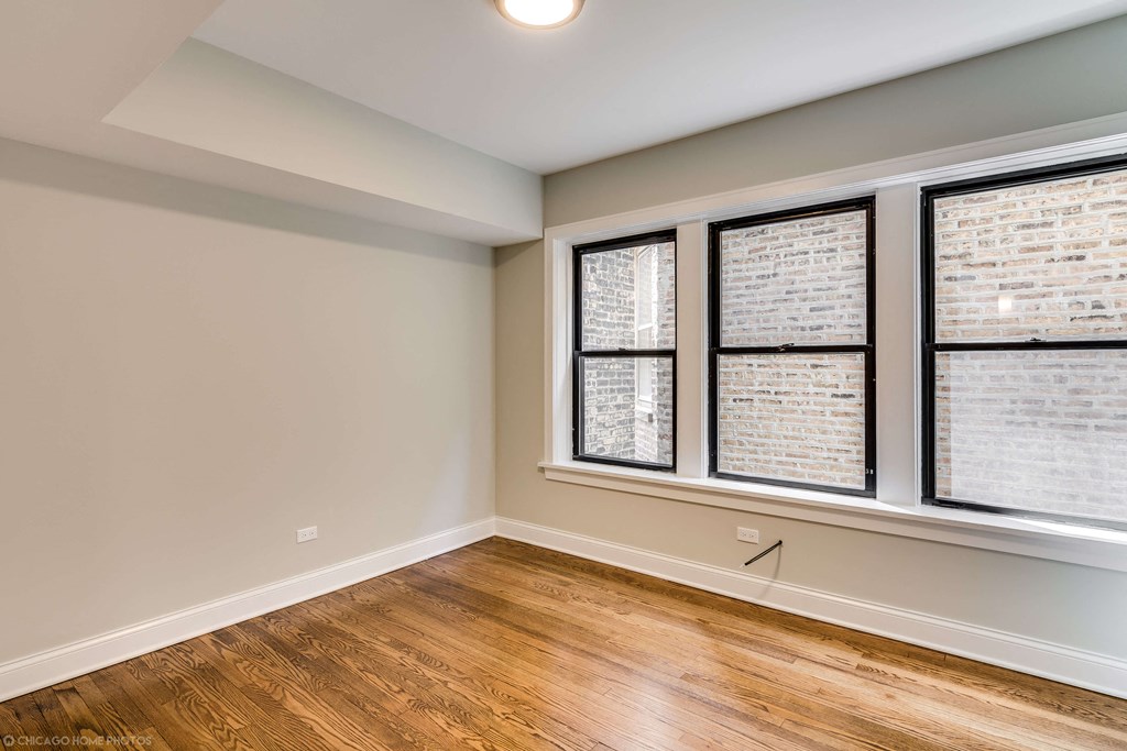 an empty living room with three windows and wood floors