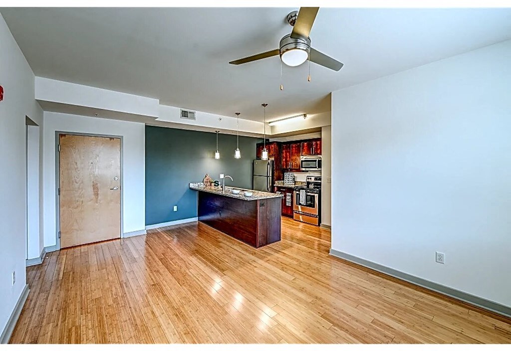 an empty living room with a kitchen and a ceiling fan