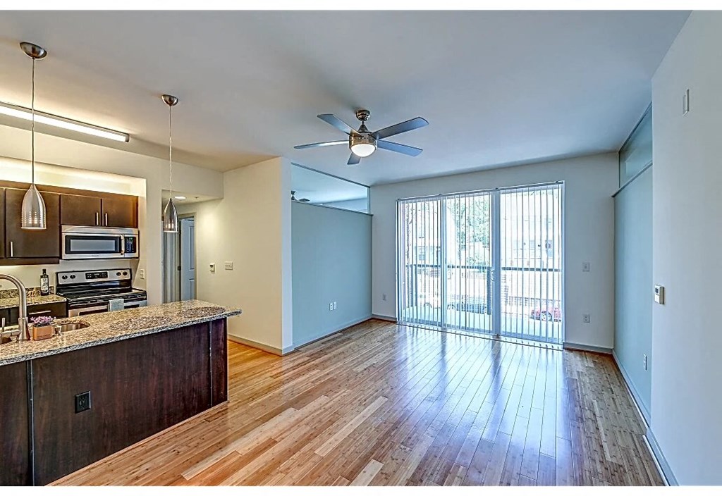 an empty living room with a kitchen and a ceiling fan