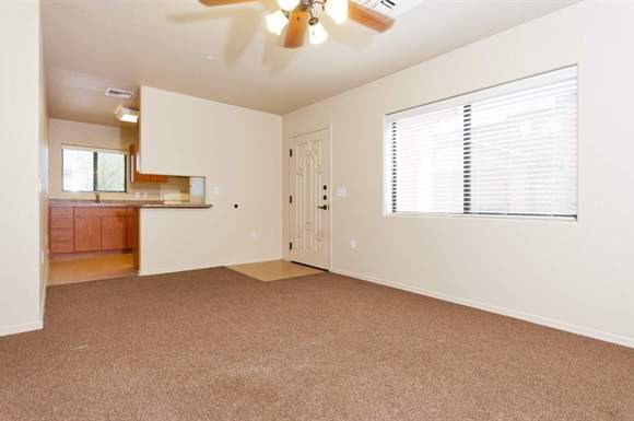 an empty living room with a kitchen and a ceiling fan