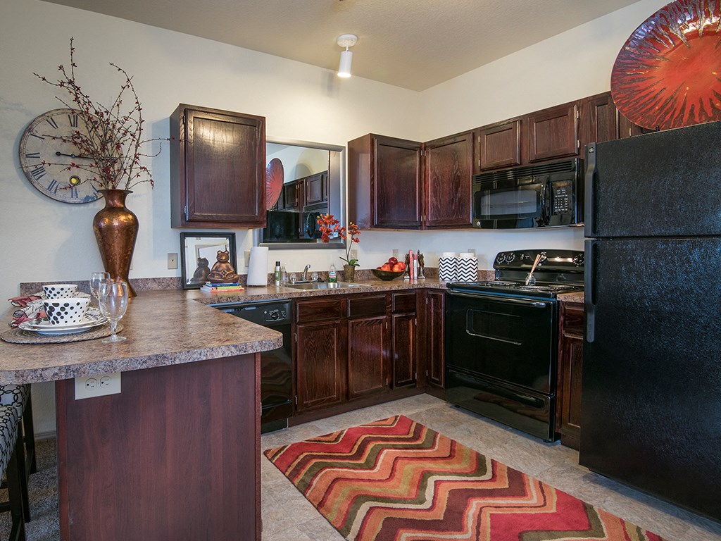 a kitchen with black appliances and wooden cabinets and a rug