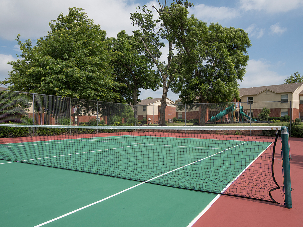a tennis court with trees and apartments in the background