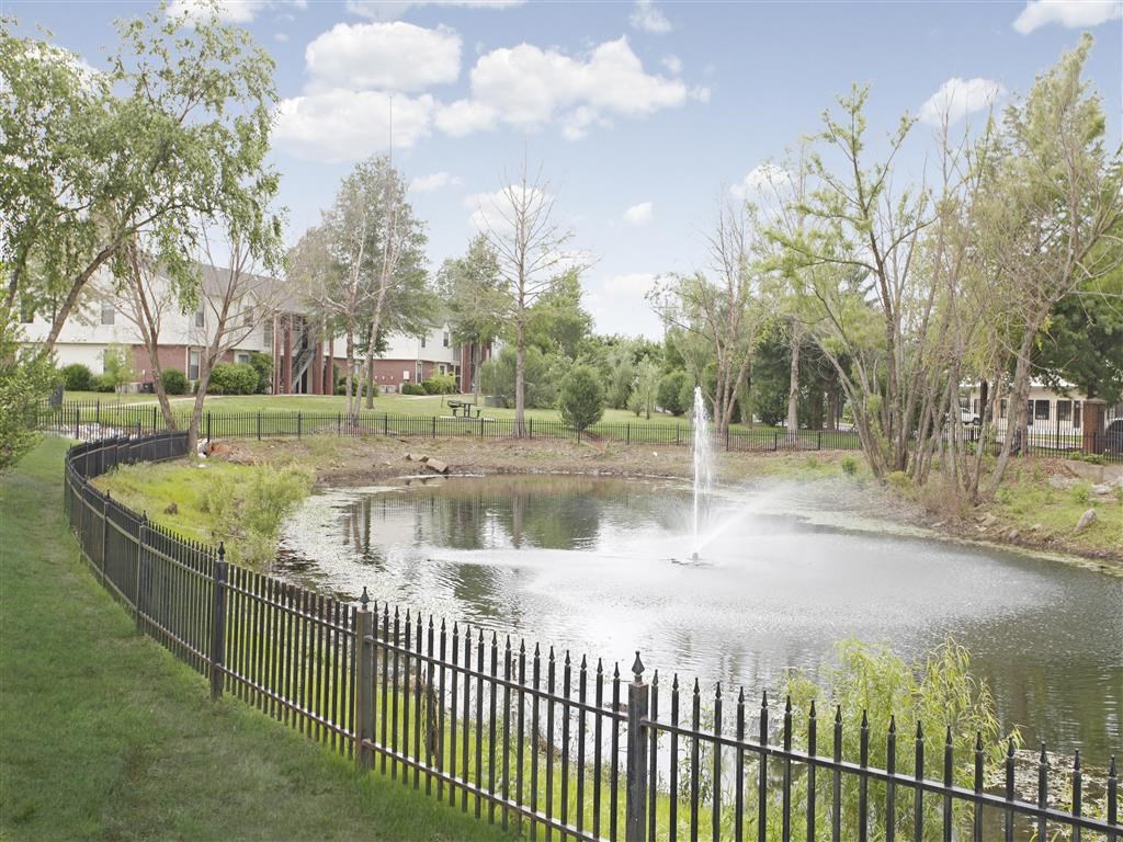 a pond with a fountain in a park with a fence