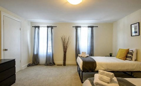 A bedroom with a bed, dresser, and window with curtains.