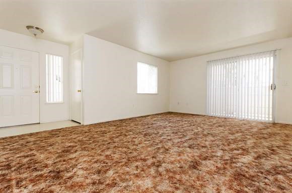 an empty living room with white walls and a brown carpet