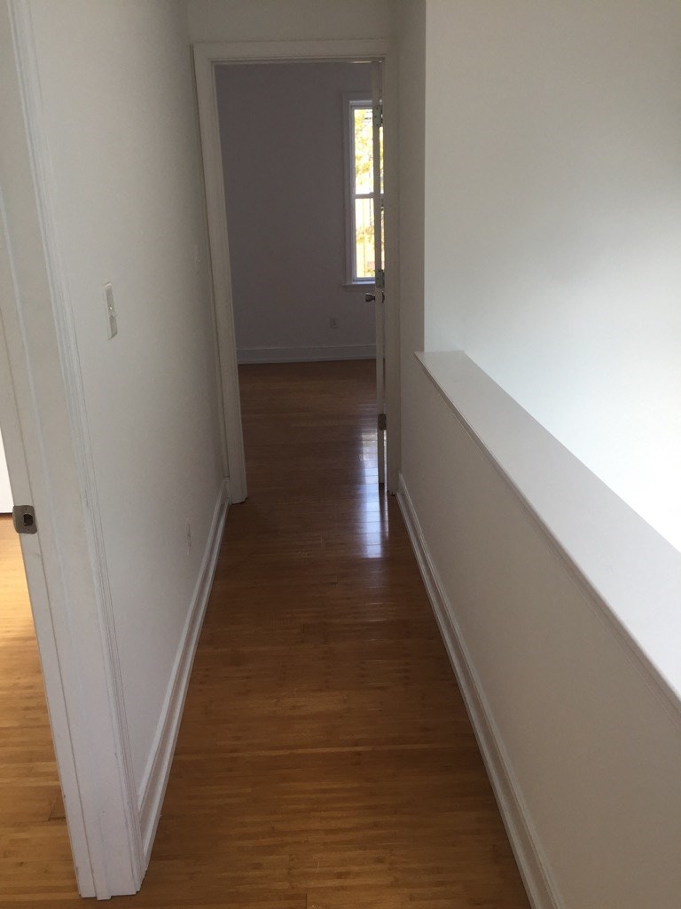 a hallway with white walls and a wooden floor and a window