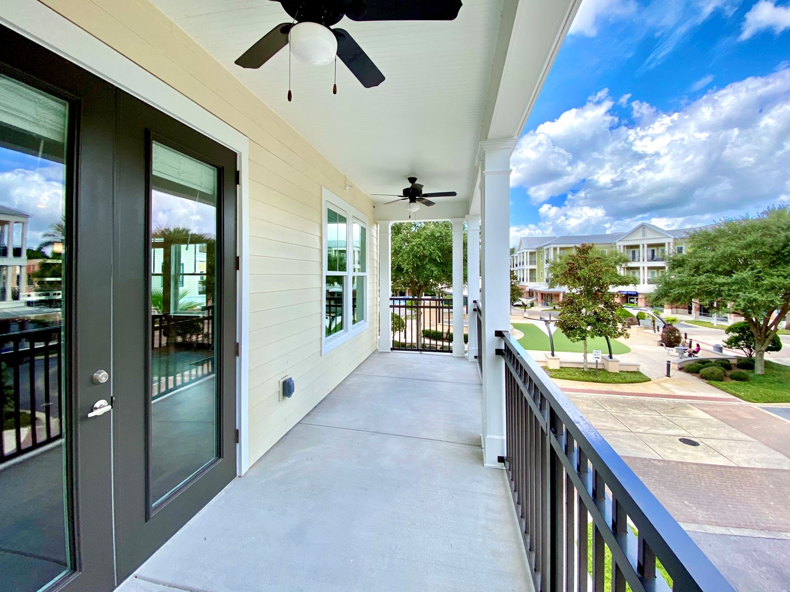 A large covered outdoor apartment balcony with two ceiling fans, and beautiful views of trees, grass, and the community.