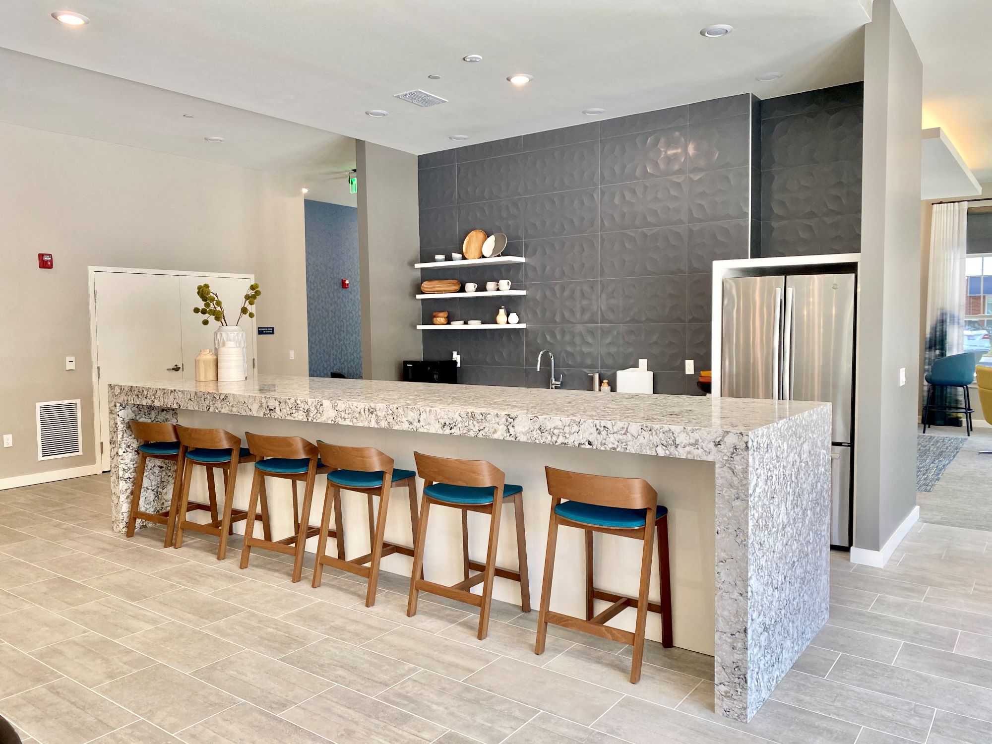 A community clubhouse kitchen with a long bar, a refrigerator, a sink, and six barstools.