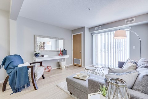 A living room with a grey couch, a white coffee table, a blue chair, and a mirror on the wall.