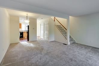 an empty living room with a staircase and a kitchen