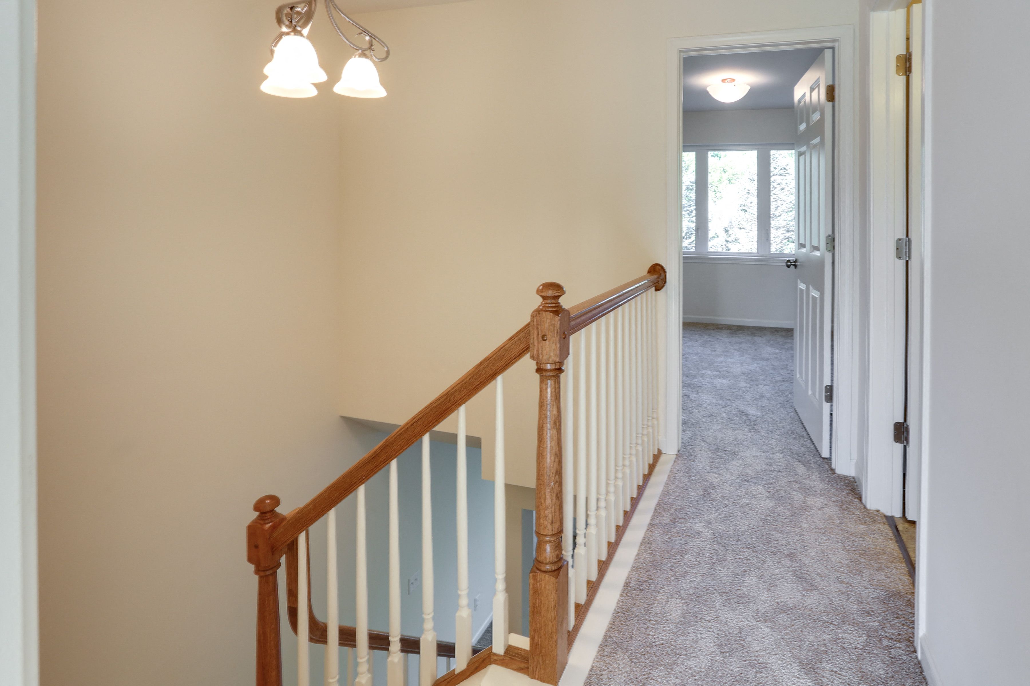 the landing of a staircase in a home with white carpet and a hallway with stairs