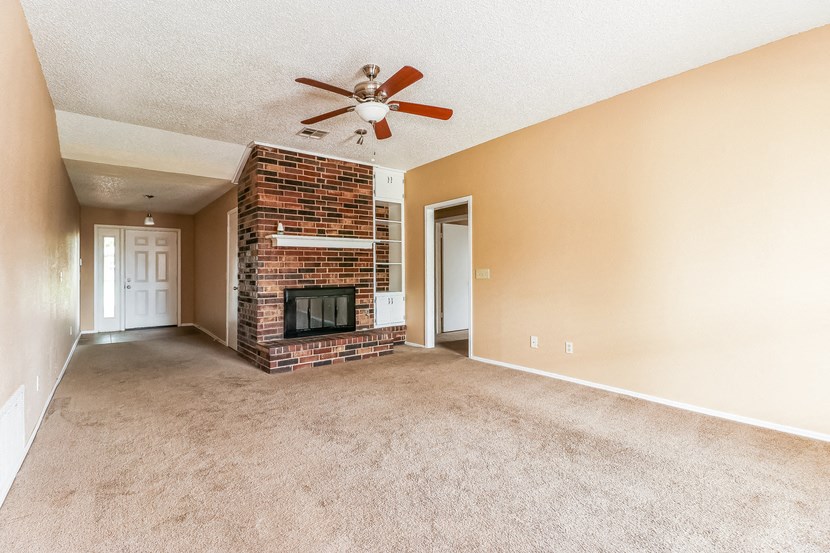 an empty living room with a fireplace and a ceiling fan