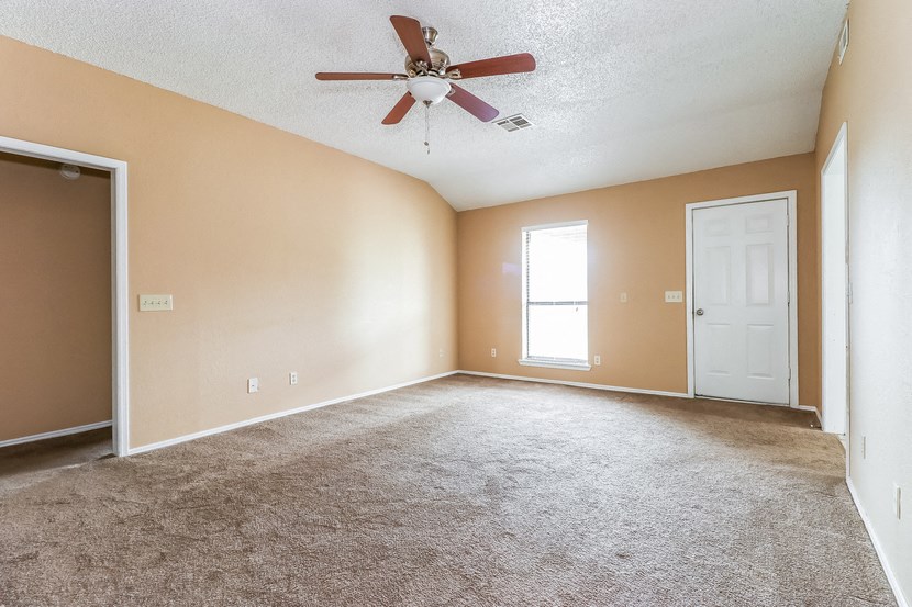 an empty living room with a ceiling fan and a door