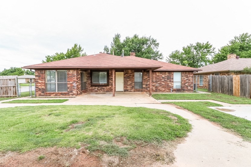 a small brick house with a yard and a wooden fence