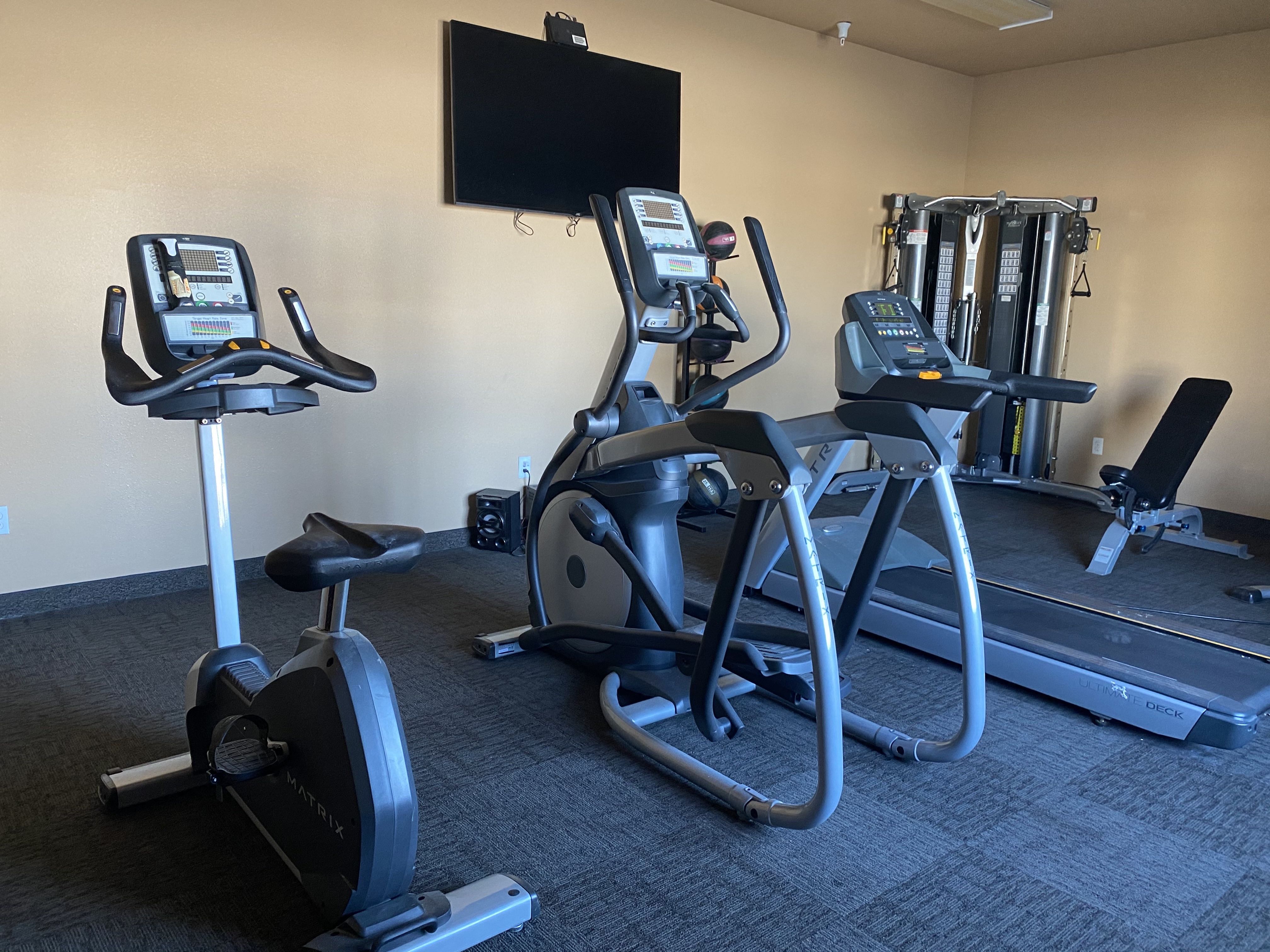 a gym with cardio equipment and a tv