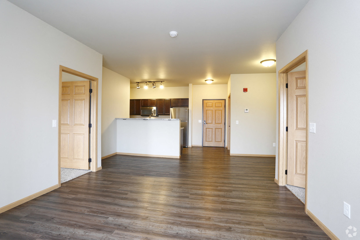 an empty living room and kitchen with wood floors and white walls