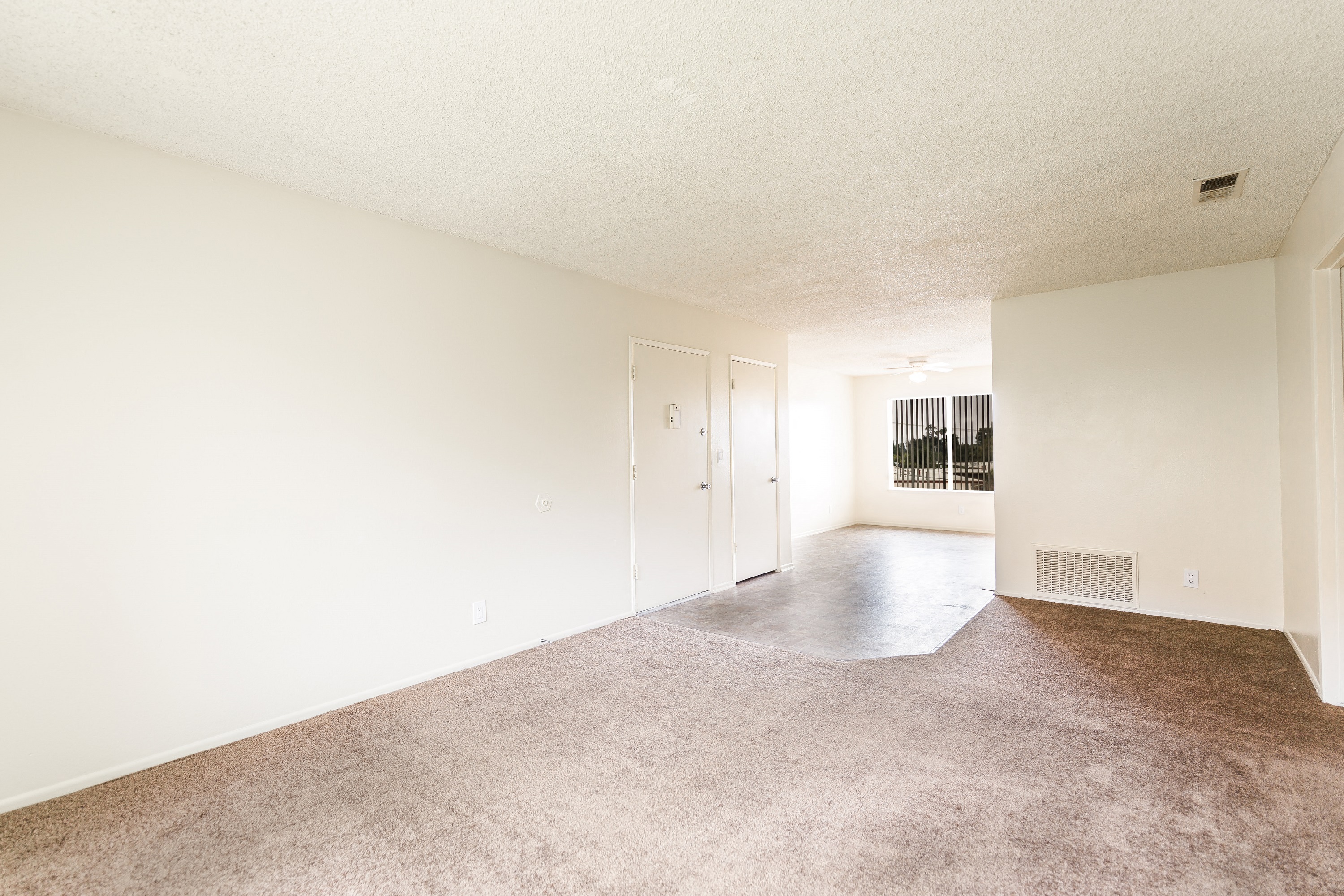 the spacious living room and dining room of an apartment with white walls and carpet