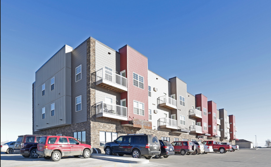 a row of apartment buildings with cars parked in a parking lot