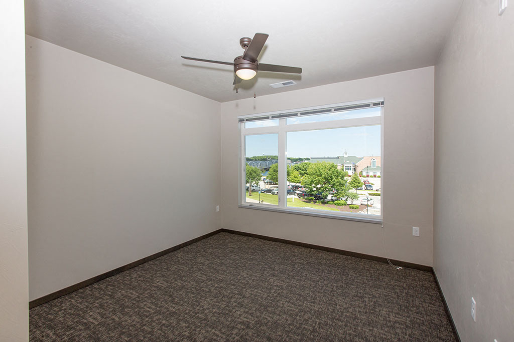 an empty living room with a large window and a ceiling fan