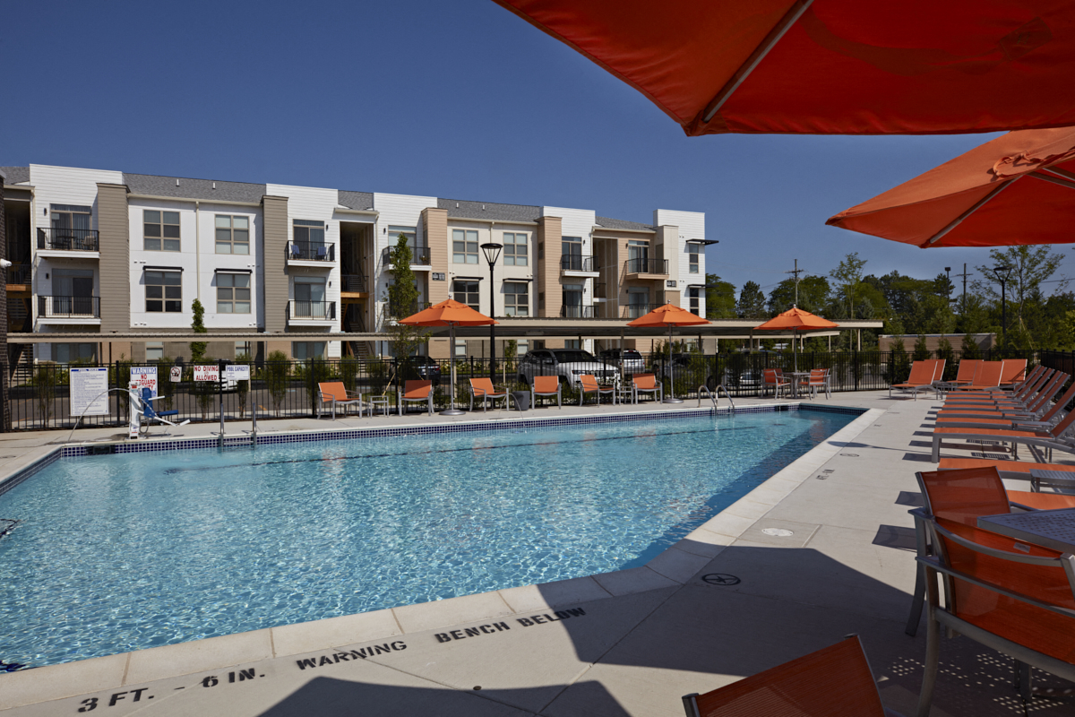 a swimming pool with chairs and umbrellas in front of an apartment building