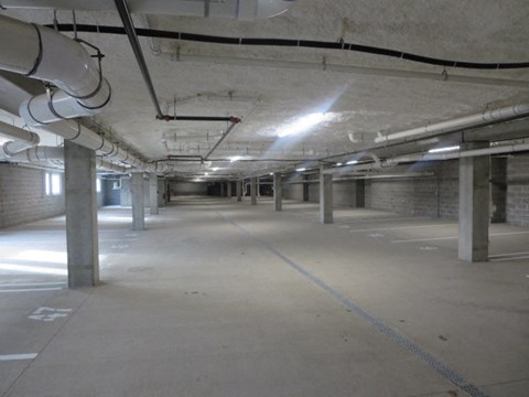 A spacious underground parking garage with concrete pillars and bright lighting.