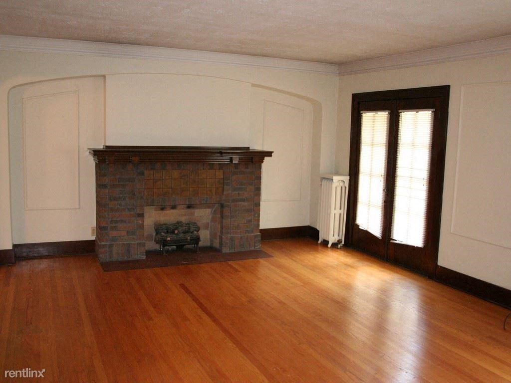 an empty living room with a brick fireplace and wooden floors